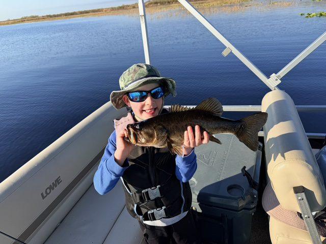 Young angler holding a largemouth bass caught from the pontoon on West Lake Toho